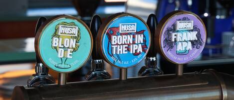 A bar with three taps labeled 'NUSA Blondie,' 'NUSA Born in the IPA,' and 'NUSA Frank APA.'