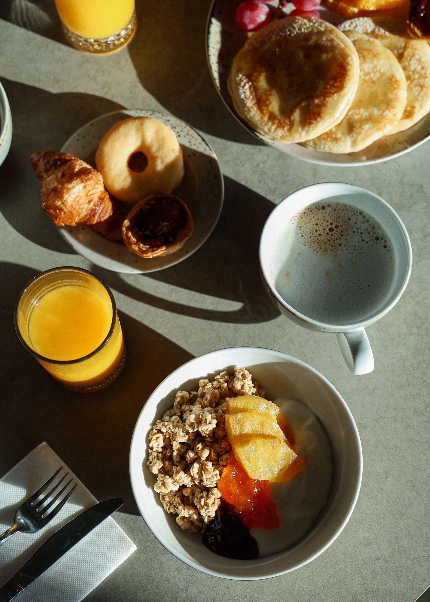 A breakfast table with pancakes, croissants, fruit, and a glass of orange juice.
