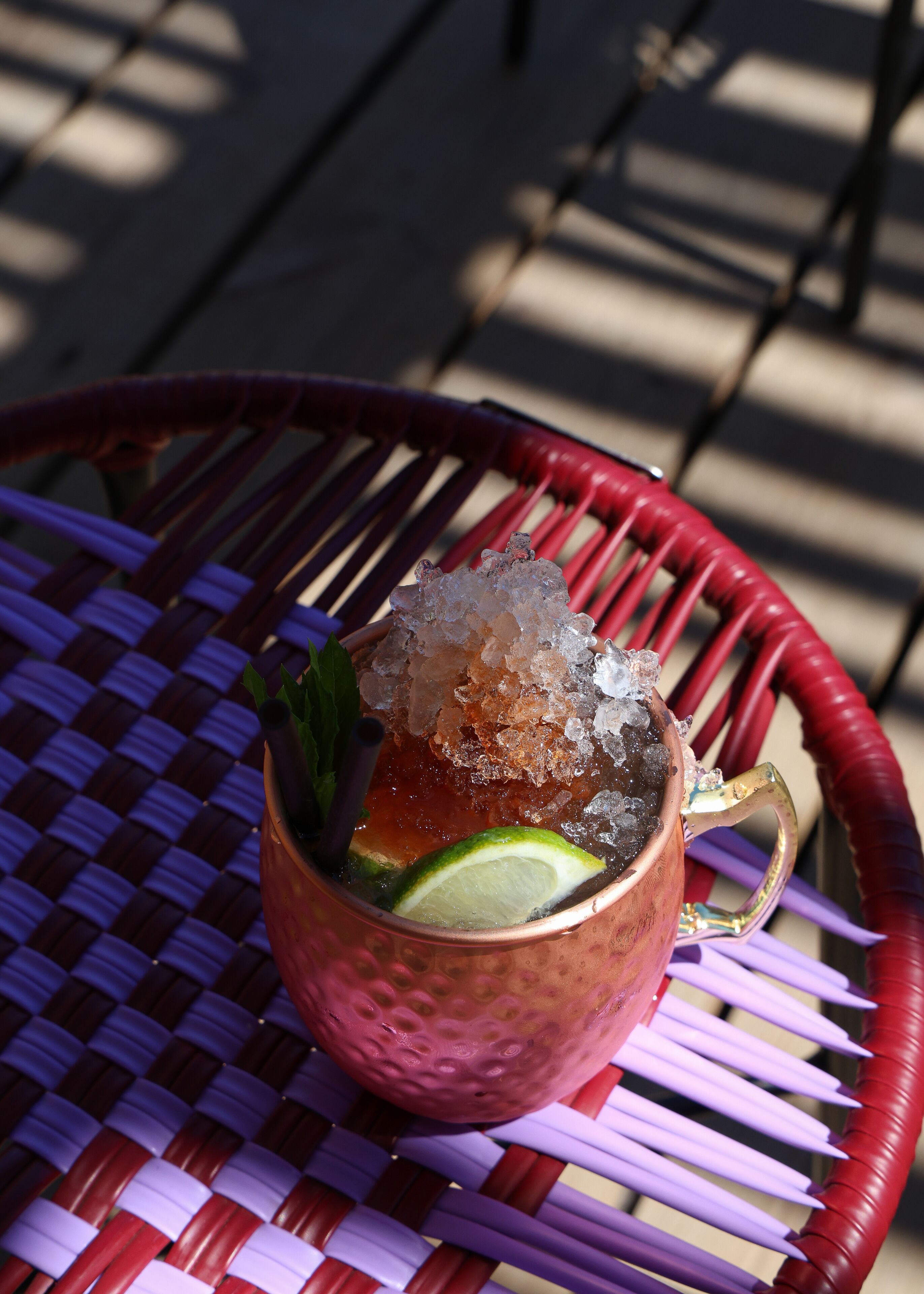 Un vaso de cobre con hielo, lima y menta sobre una mesa tejida.