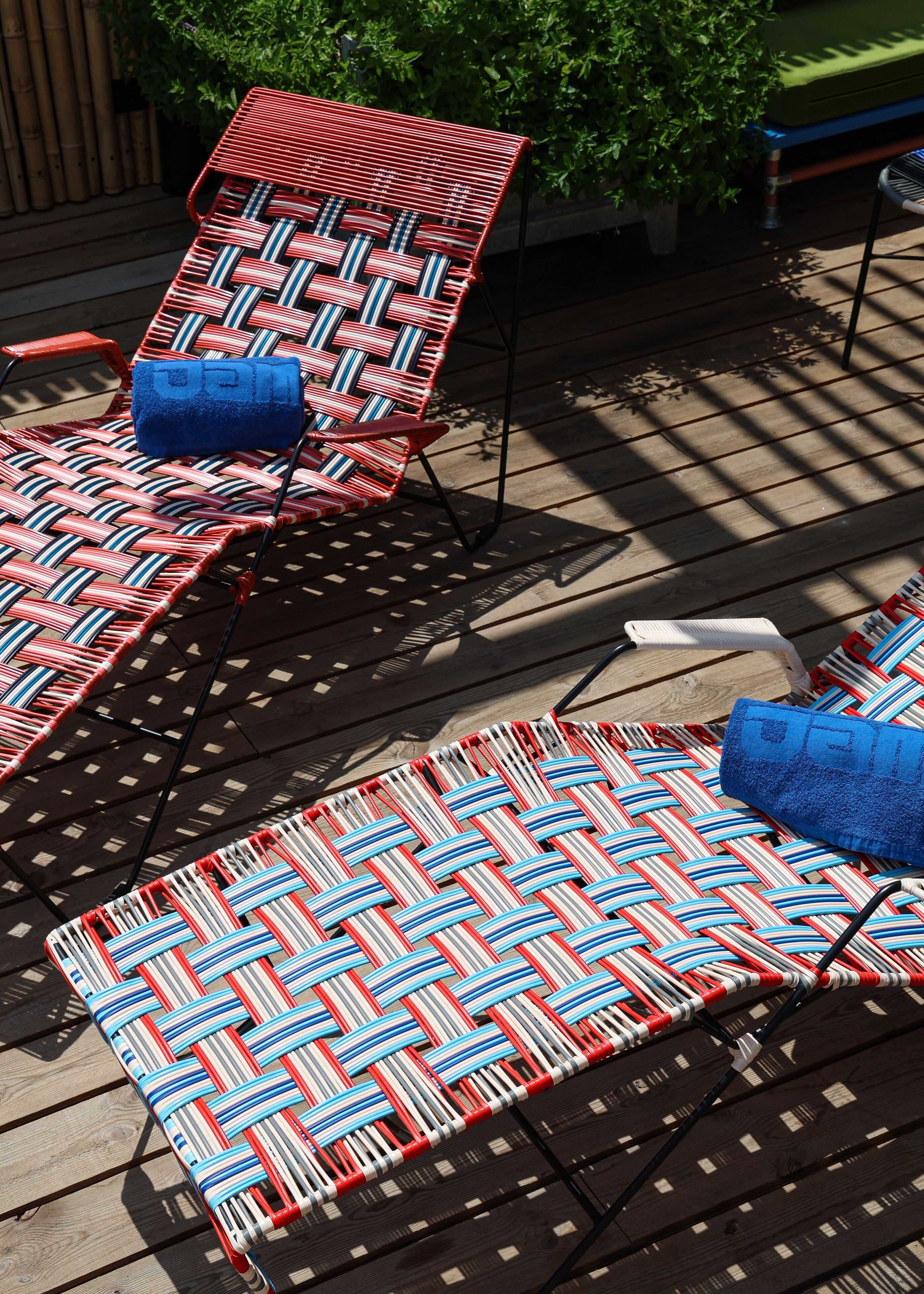 Deux fauteuils de jardin à rayures rouges et blanches, dotés de coussins bleus, disposés sur une terrasse en bois.