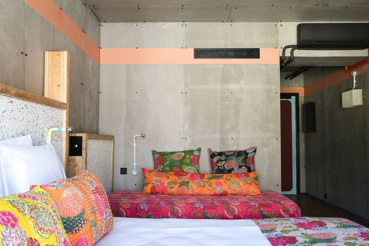 A modern bedroom with a concrete wall, a wooden headboard, and colorful bedding.