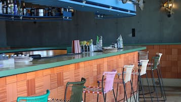 Zona de bar con una barra larga, varios taburetes y un techo de madera rústica.