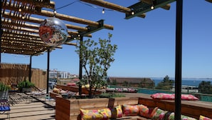 A wooden deck with colorful cushions, a disco ball, and a view of the sea. - Jam Hotel Lisbon (Lisbon)
