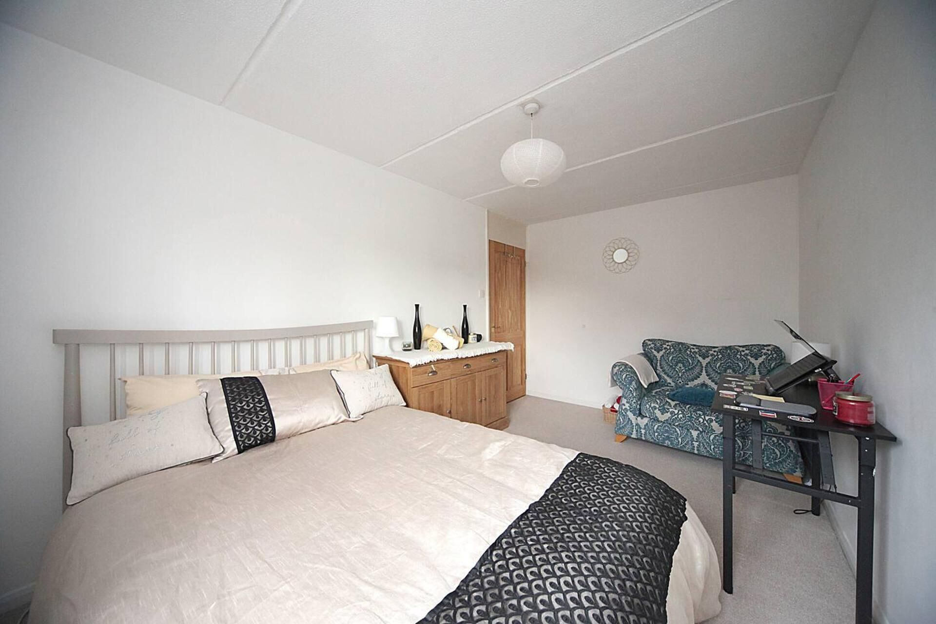 A bedroom with a bed, a dresser, a chair, and a desk with a keyboard and other items.