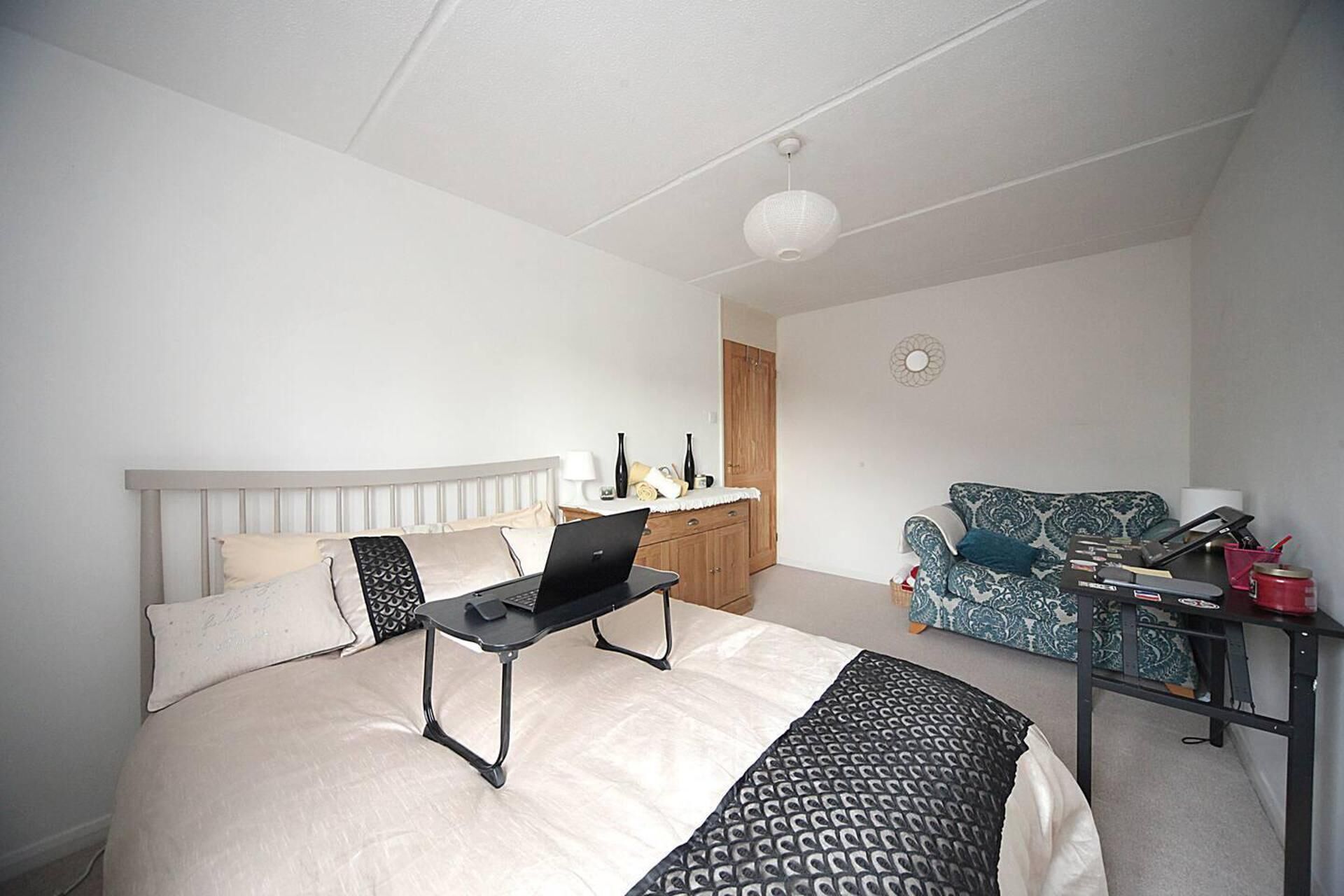 Une chambre à coucher avec un lit, un bureau, un ordinateur portable, un canapé et une armoire.