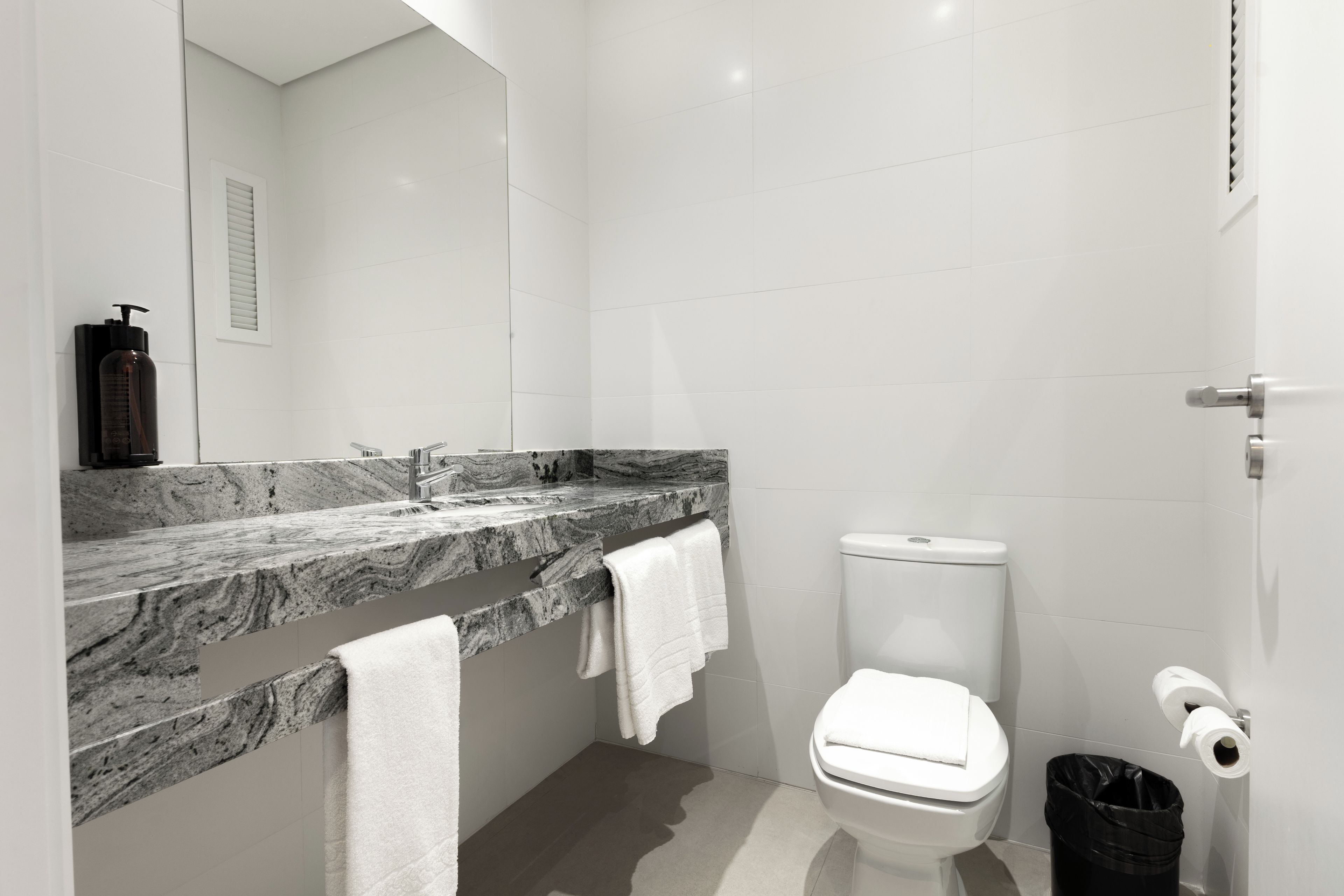 A modern bathroom with a marble countertop, a white toilet, and a black trash bin.