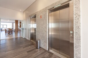 A modern elevator area with two elevators, a trash bin, and a glass door leading to a dining area.