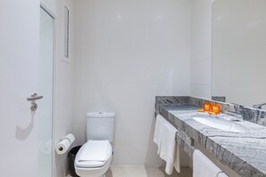 A modern bathroom with a toilet, sink, and glass shower enclosure. - Tri Hotel Executive Osório (Osorio)