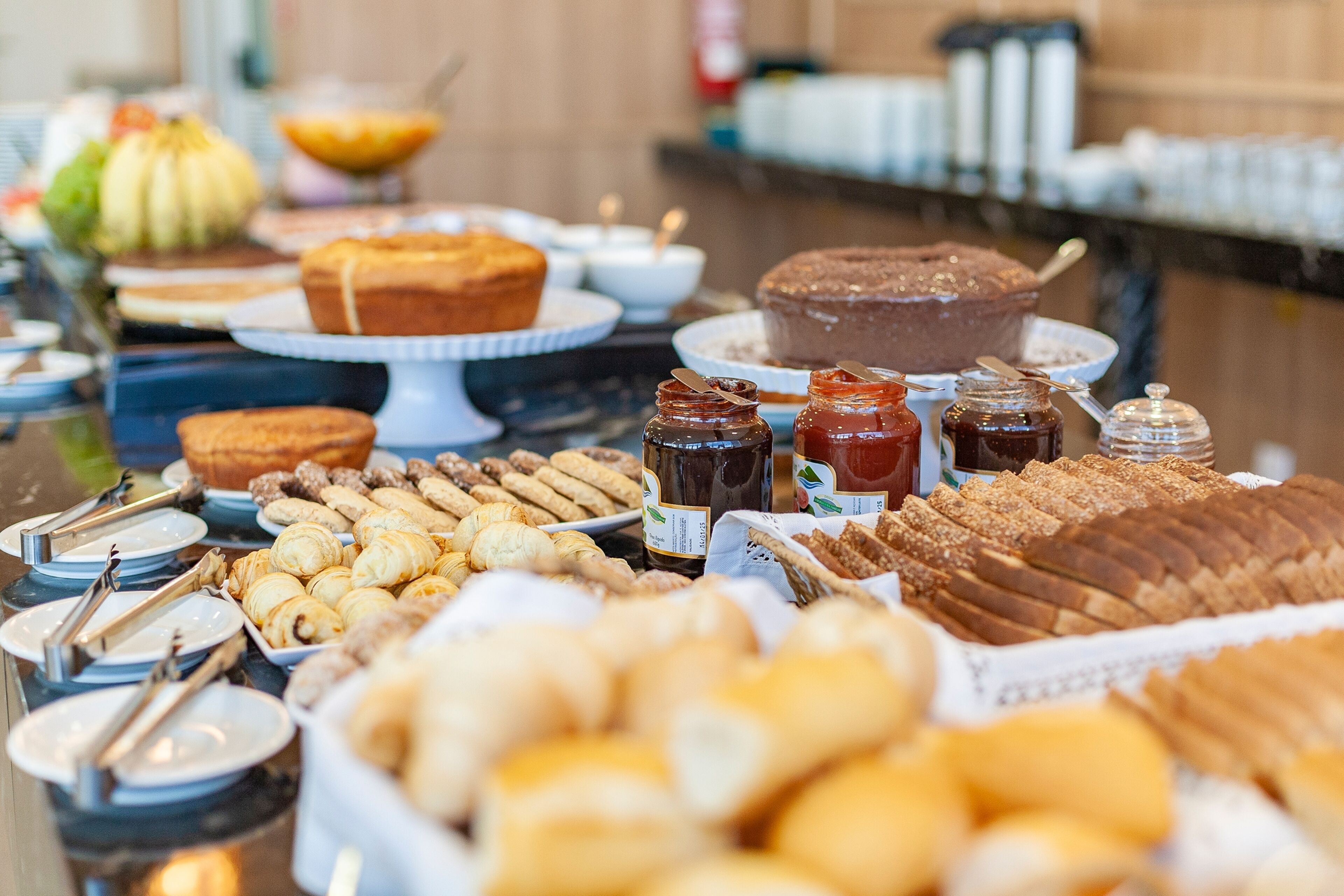 Buffet com diversos pães, doces e acompanhamentos.