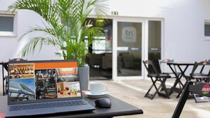 Una laptop sobre una mesa con una taza de café y un ratón, una planta y una vista de un edificio con un letrero que dice "tri".