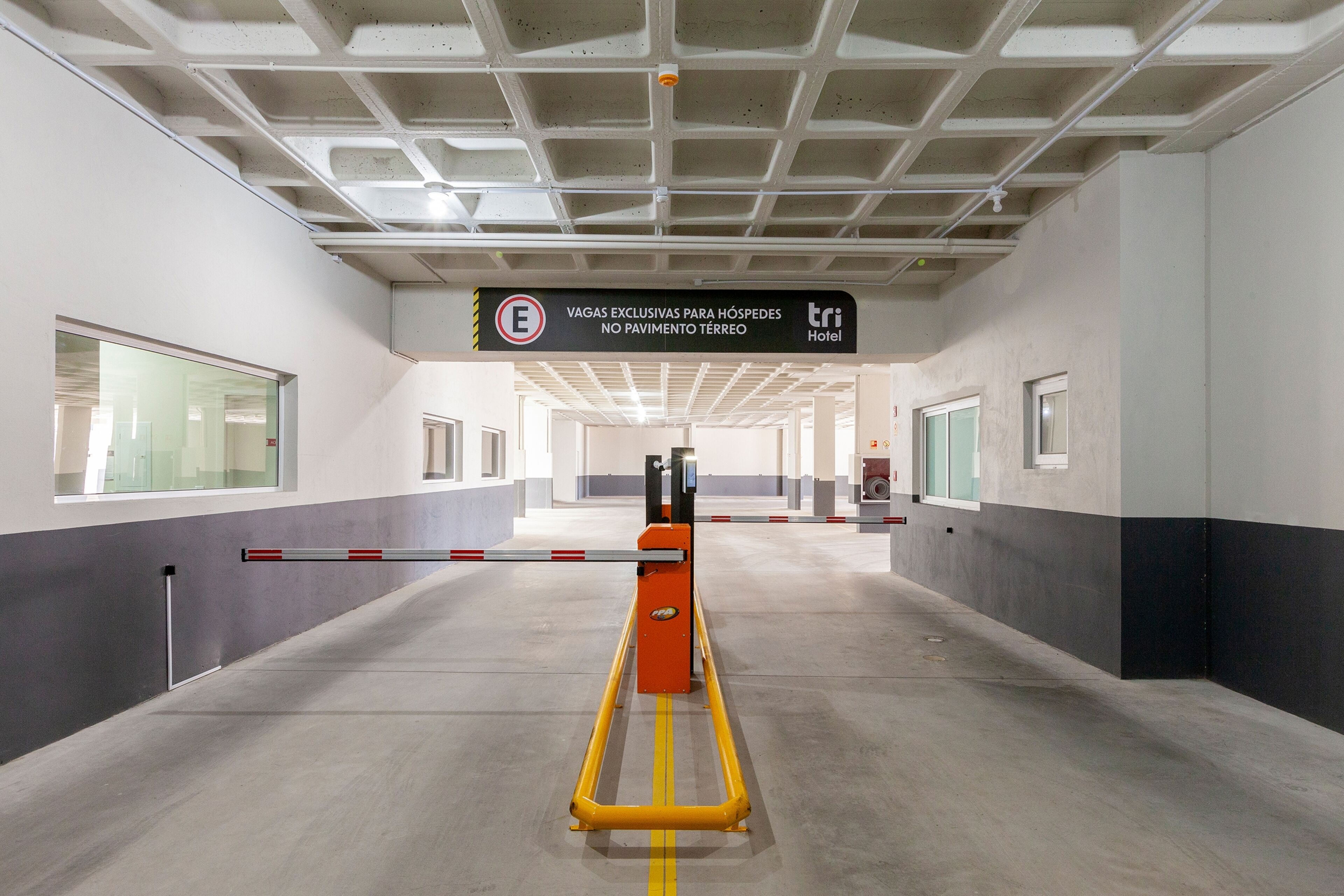 Entrada de hotel com portão de segurança, placa indicando acesso exclusivo para hóspedes e design moderno no teto.