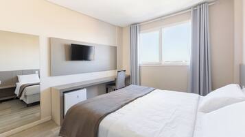 Habitación de hotel con cama, escritorio, silla, televisor montado en la pared y ventana con cortinas.