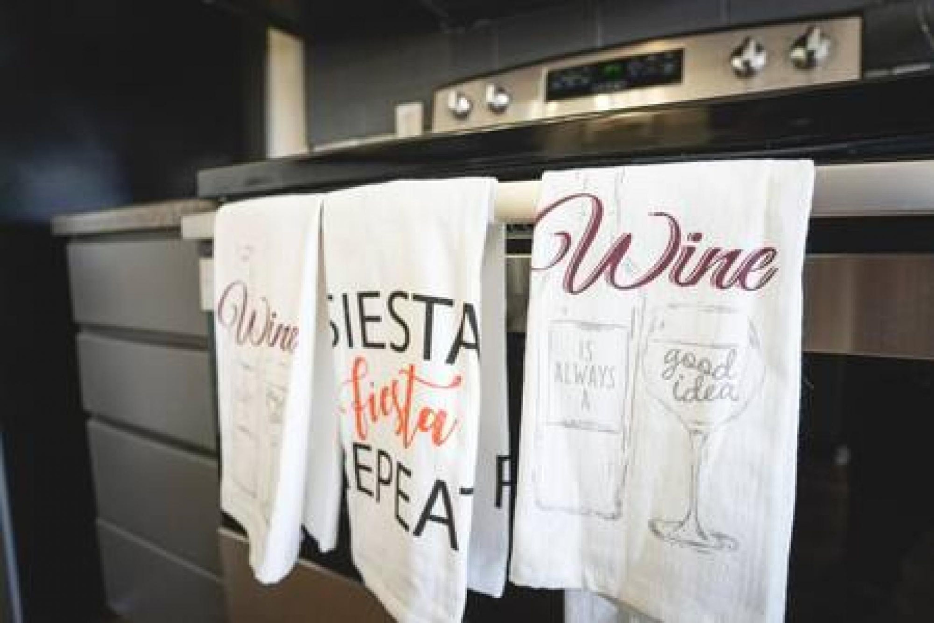 Kitchen towels hanging on a rack with text related to wine and a fiesta.