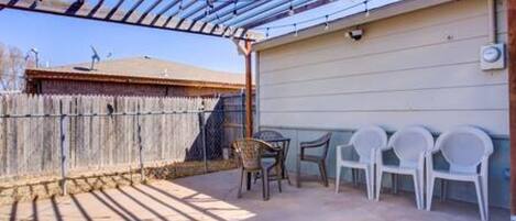 Um pátio externo com pérgola, cerca de madeira e cadeiras de plástico.