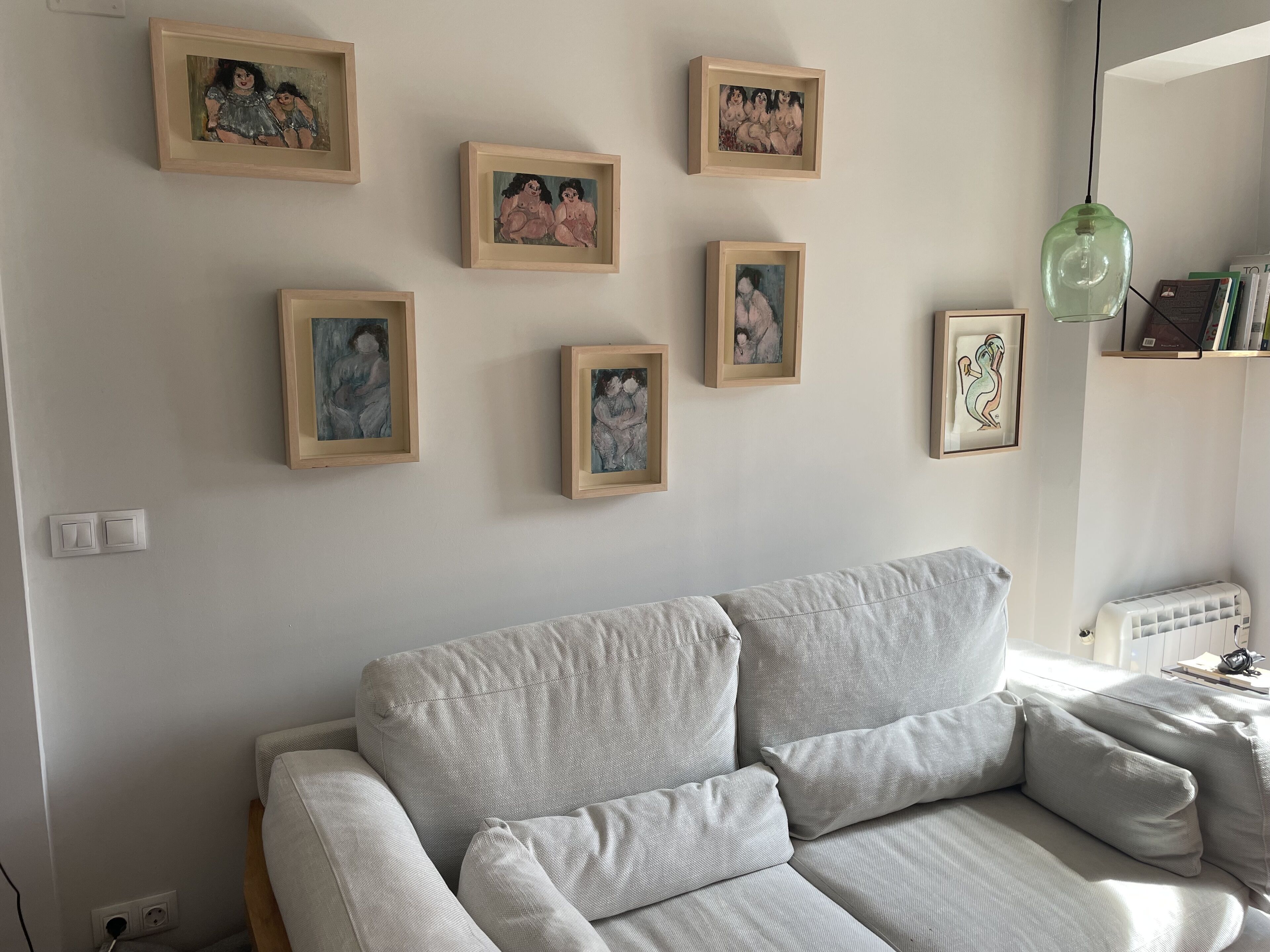 A living room with a grey sofa, a green pendant light, and several framed artworks on the wall.