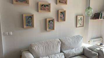 A living room with a grey sofa, a green pendant light, and several framed artworks on the wall.