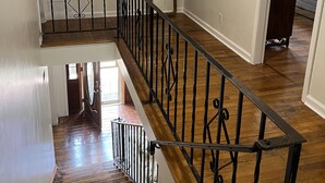 Een trap met houten bekleding en een zwarte metalen balustrade, leidend naar een slaapkamer met een bed en een ladekast.