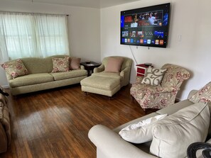 Una sala de estar con televisión de pantalla plana montada en la pared, un sofá, un reposapiés y un sillón estampado.