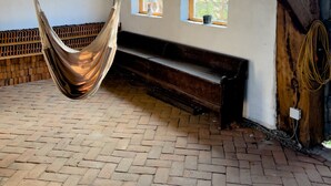 A hammock suspended from the ceiling in a rustic room with brick flooring, wooden beams, and arched windows. - Viscri 9 (Bunesti)