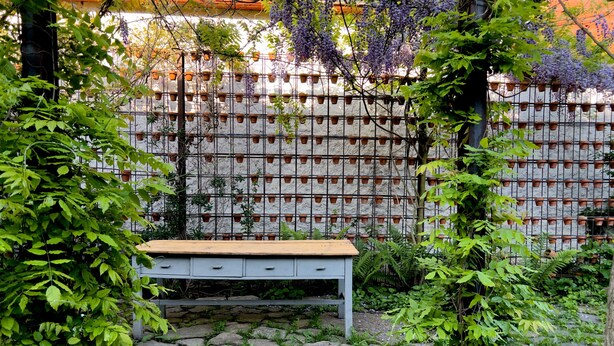 A stone bench in a garden with a metal fence and potted plants. - Viscri 9 (Bunesti)