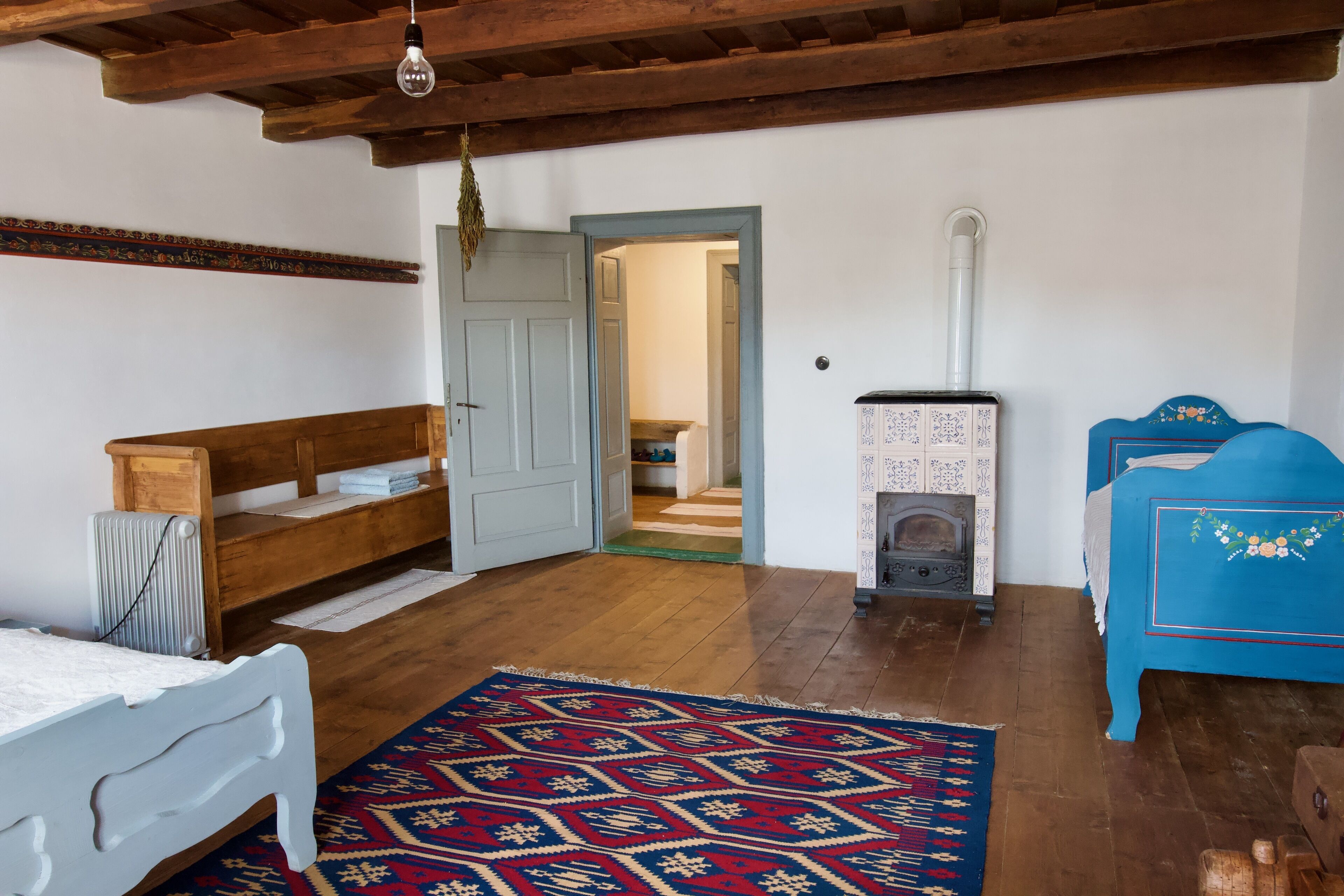 Une pièce comprenant un banc en bois, un lit, un canapé bleu, un tapis à motifs et un poêle à bois.