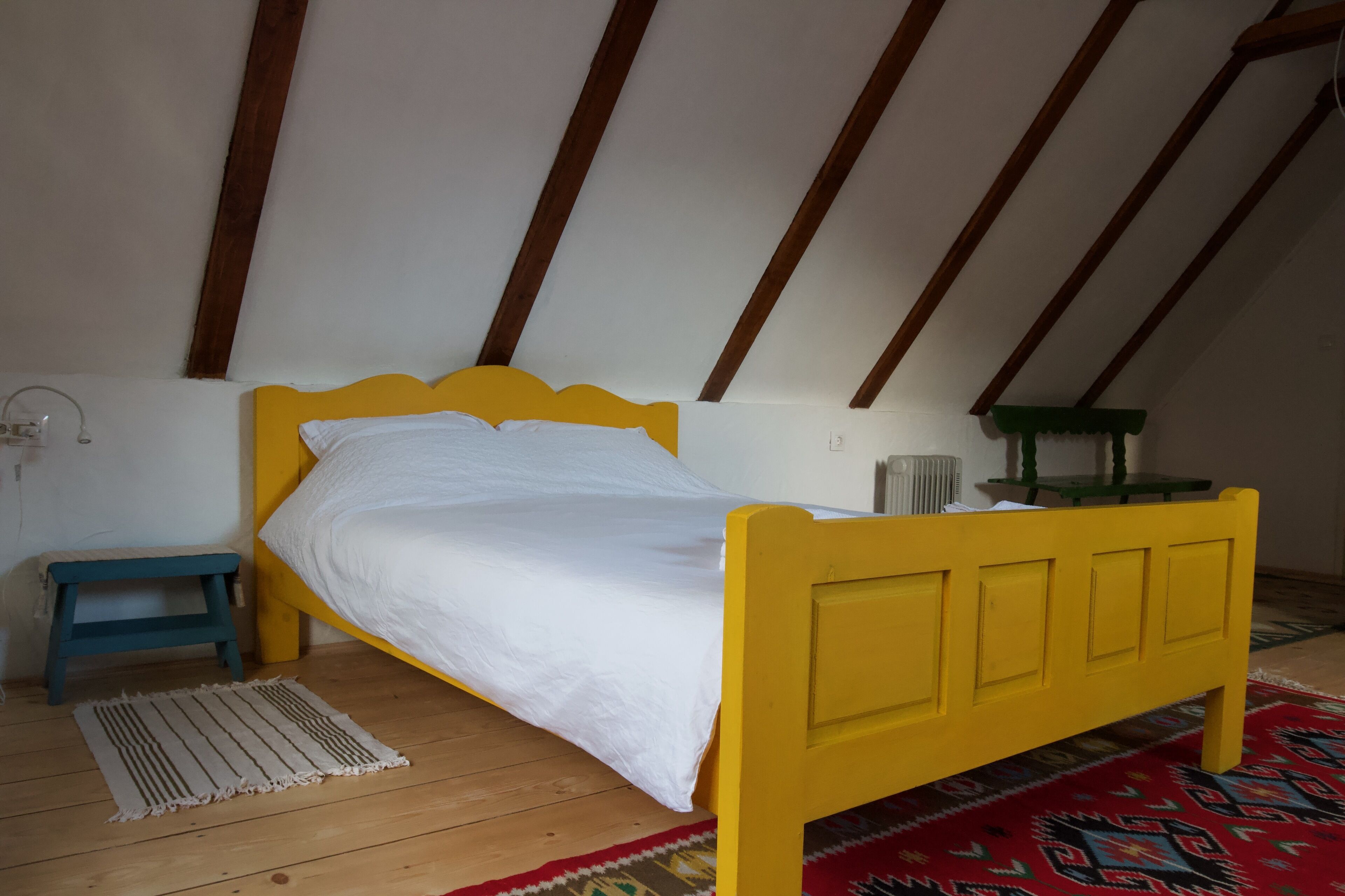 A room with a yellow bed, a small blue stool, a white rug, and a red patterned rug.