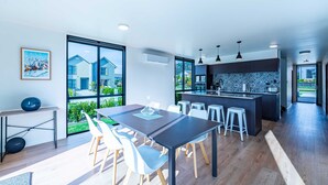 A modern kitchen with a large island, white bar stools, and a dining area with a table and chairs. - Amazing Alpine Views in Wanaka (Wānaka)