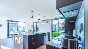 A modern kitchen with a central island, built-in appliances, and large windows offering views of the outdoors. - Amazing Alpine Views in Wanaka (Wānaka)