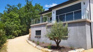 A modern building with a balcony, a small tree, and a gravel path. - Maison Avec Piscine, Dans un Quartier Calme Sans vis à Vis, Près D'une Forêt (Saint-Julien-de-Peyrolas)