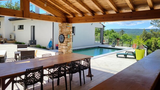 A covered outdoor area with a pool, stone pillar, and dining setup. - Maison Avec Piscine, Dans un Quartier Calme Sans vis à Vis, Près D'une Forêt (Saint-Julien-de-Peyrolas)