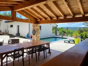 A covered outdoor area with a pool, stone pillar, and dining setup. - Maison Avec Piscine, Dans un Quartier Calme Sans vis à Vis, Près D'une Forêt (Saint-Julien-de-Peyrolas)