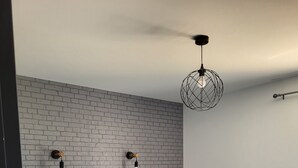 A modern bedroom with a white brick wall, a bed with a grey mattress, and a hanging light fixture. - Maison Avec Piscine, Dans un Quartier Calme Sans vis à Vis, Près D'une Forêt (Saint-Julien-de-Peyrolas)