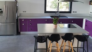 A modern kitchen with a central island, purple cabinets, and a stainless steel refrigerator. - Maison Avec Piscine, Dans un Quartier Calme Sans vis à Vis, Près D'une Forêt (Saint-Julien-de-Peyrolas)