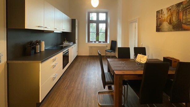 Une cuisine moderne avec un coin repas, un plancher en bois et une grande fenêtre qui laisse entrer la lumière naturelle.