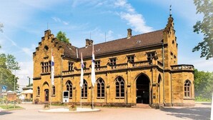 Un bâtiment historique doté d’une entrée centrale en arc de cercle, de nombreuses fenêtres et d’une tour imposante surmontée d’une flèche.