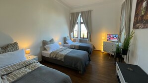 Une chambre d’hôtel avec deux lits, une télévision, un bureau et une fenêtre avec des rideaux.
