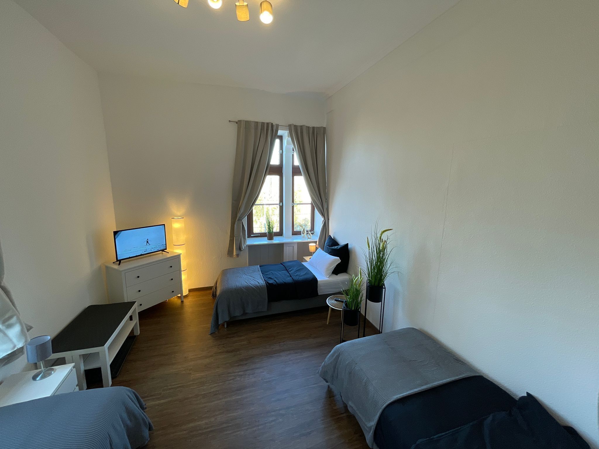A compact hotel room with a bed, bedside table, desk, and a window with curtains.