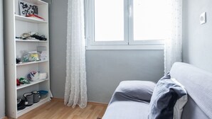 A room with a white wardrobe, a grey sofa, and a window with white curtains. - Modern apt with Increbilbe Athens Views (Galatsi)