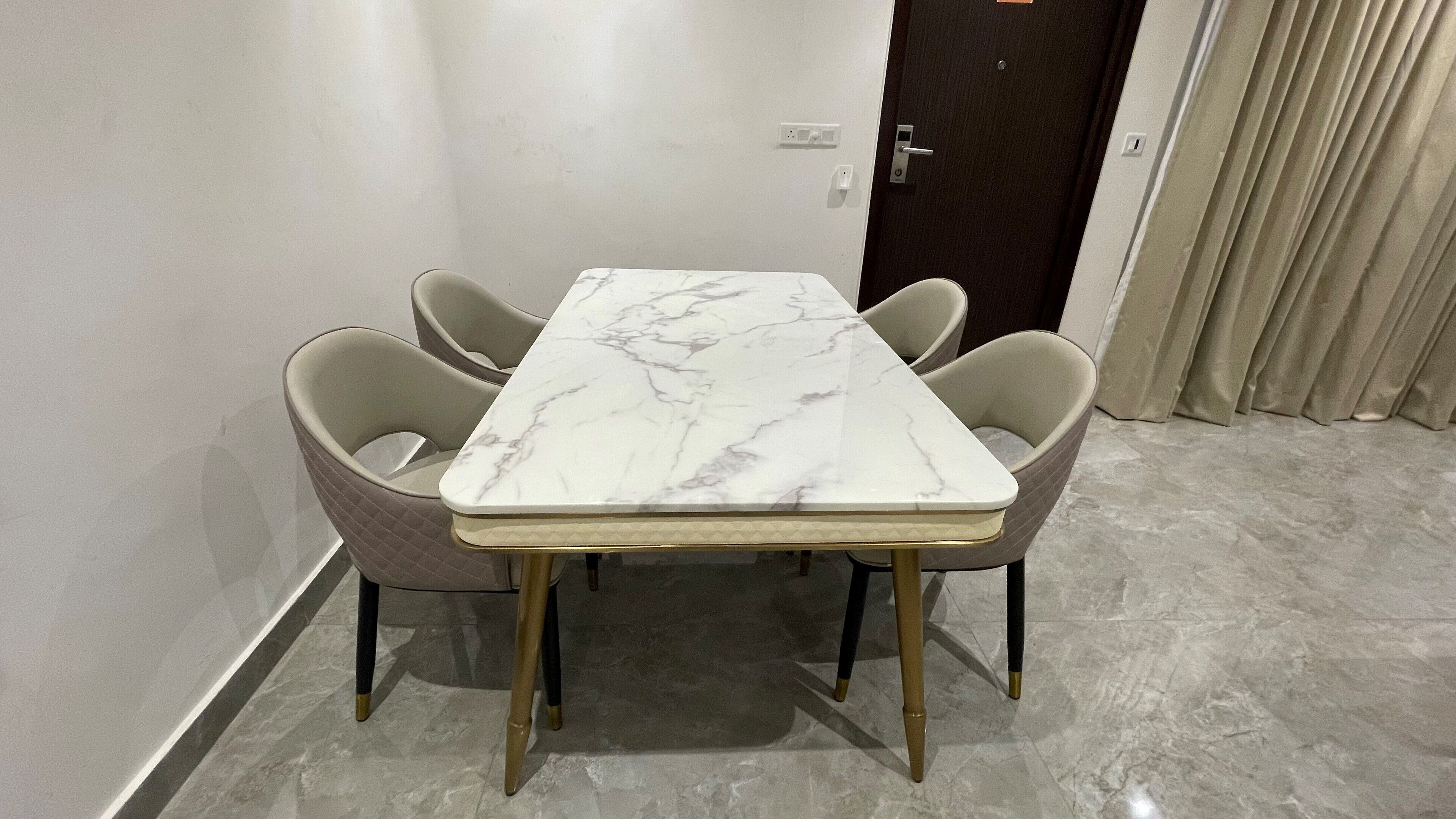 A dining table with a marble top, four cushioned chairs, and a dark door in the background.
