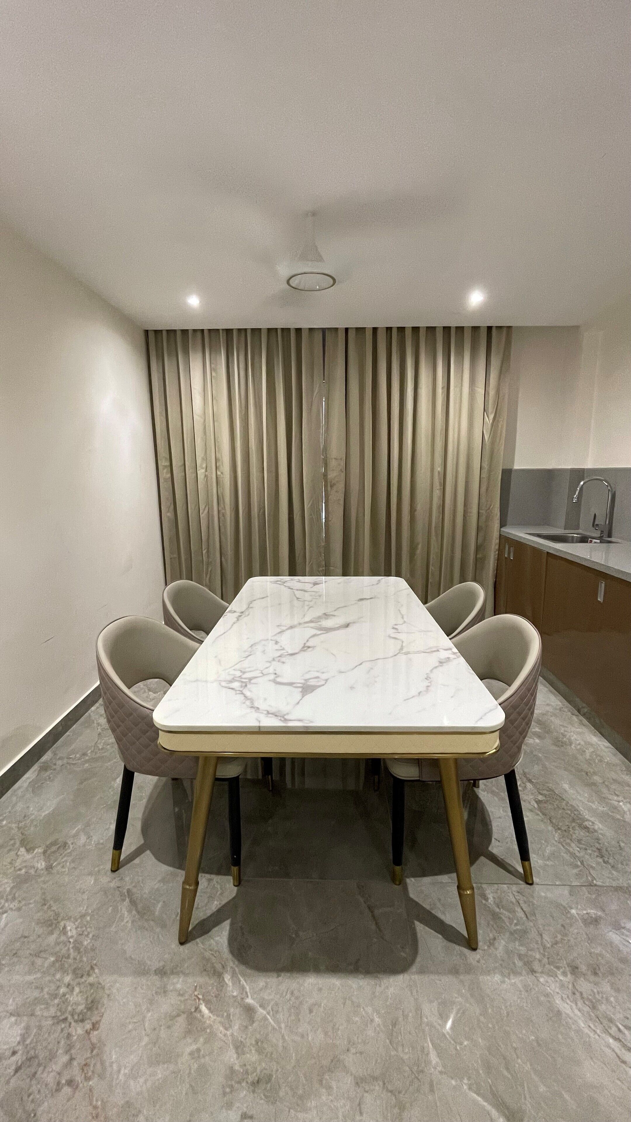 A modern dining area with a marble table, cushioned chairs, and a kitchen in the background.