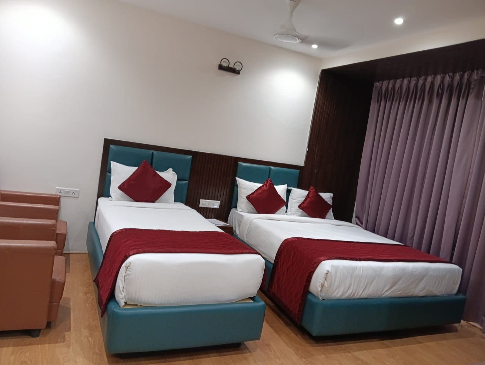 Ein Hotelzimmer mit zwei Betten, Holzboden, Deckenventilator und einem Vorhangfenster.
