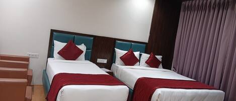 Een hotelkamer met twee bedden, een houten vloer, een plafondventilator en een raam met gordijnen.