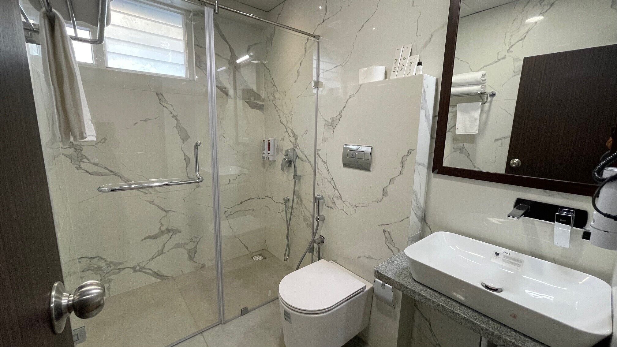 Un baño moderno con cabina de ducha de vidrio, inodoro blanco y lavamanos con encimera de mármol.