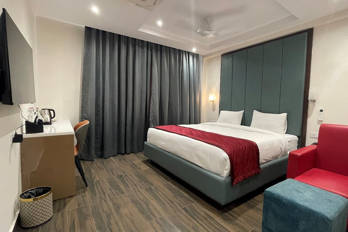 Une chambre d’hôtel avec un lit, une chaise rouge et bleue, un bureau avec une machine à café et un téléviseur.