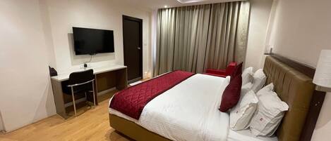 A hotel room with a bed, a desk, a chair, a television, and a window with curtains.