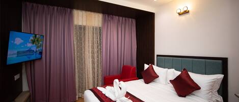 Habitación de hotel con una cama grande, televisor de pantalla plana, ventilador de techo y lámpara fijada a la pared.
