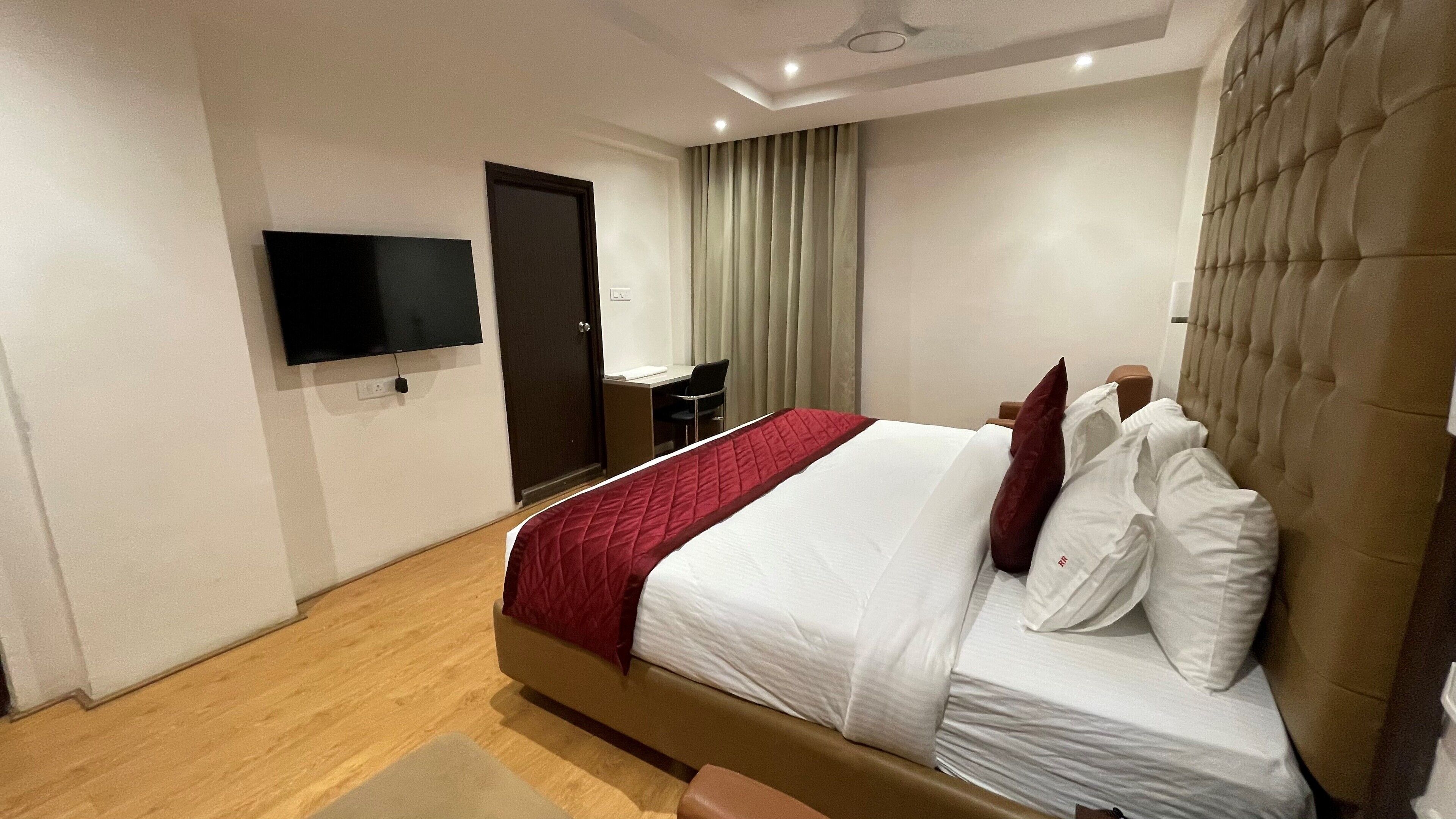 Une chambre d’hôtel avec un lit, un bureau, une chaise, une télévision et une porte.