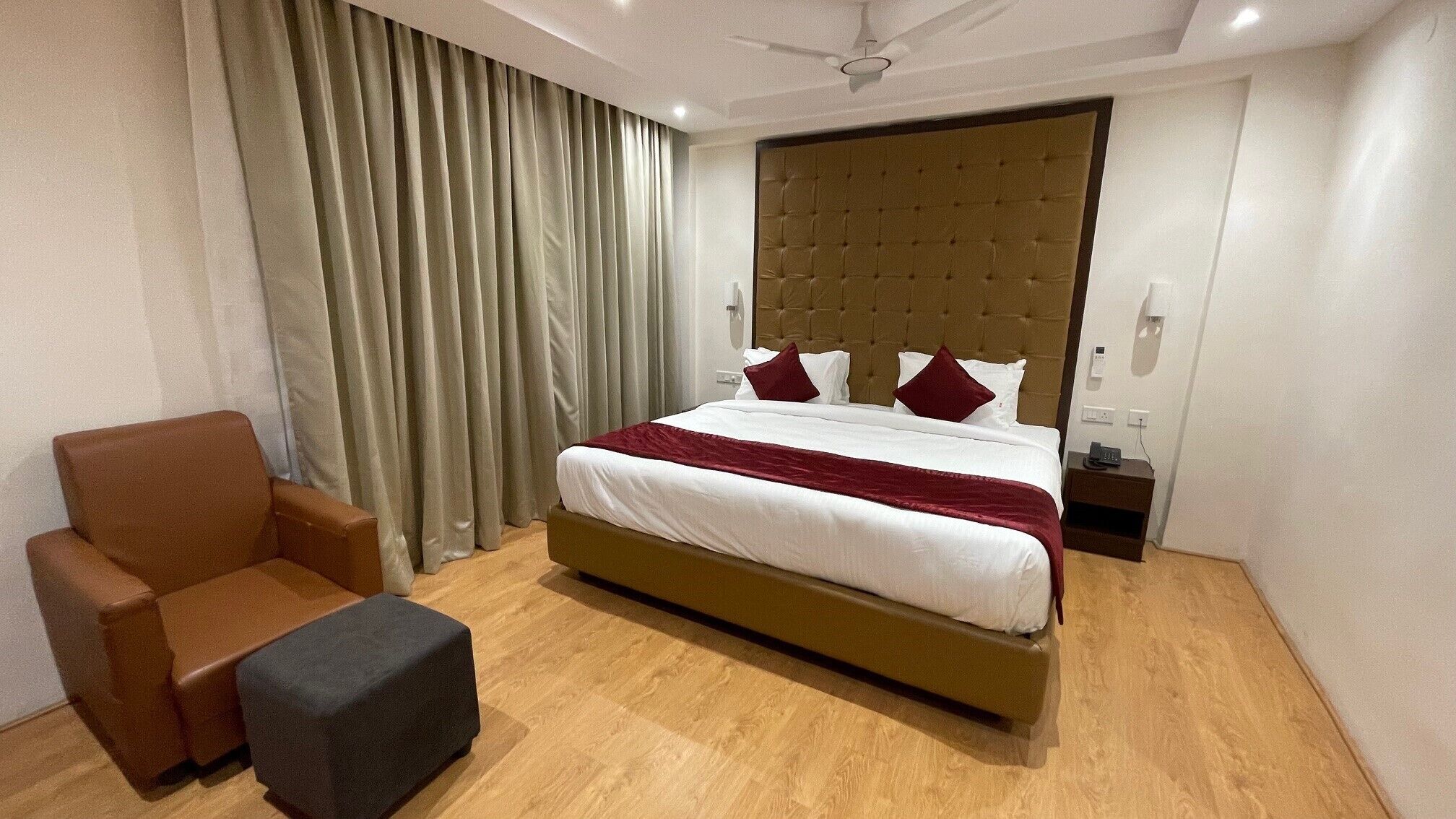 A hotel room with a large bed, a brown armchair, a small ottoman, and a nightstand with a phone.