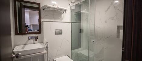 Un baño moderno con ducha envuelta en vidrio, un lavabo blanco y un espejo sobre él.