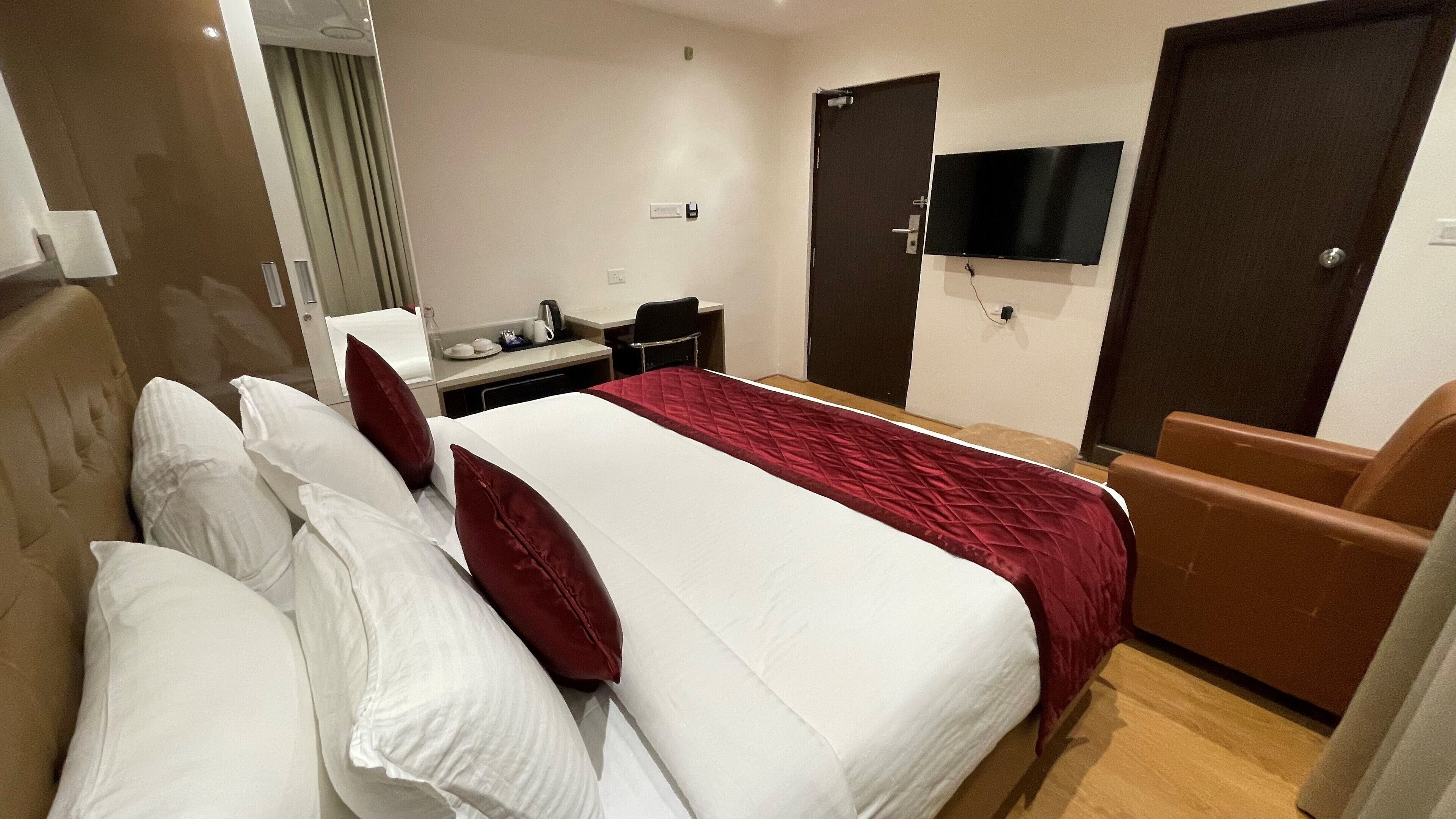 Ein Hotelzimmer mit einem großen Bett, einem Schreibtisch, einem Sessel, einem Fernseher und einer Tür.